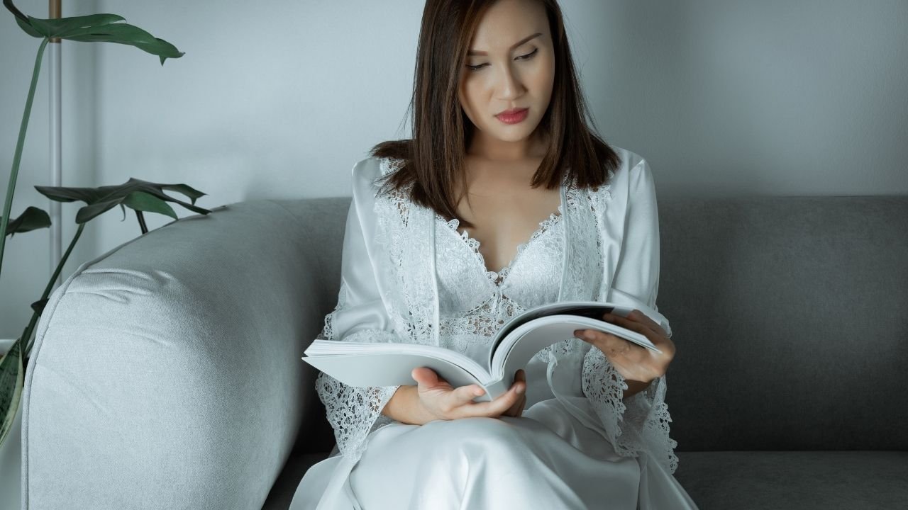 mulher com camisola oversized branca lendo livro no sofá