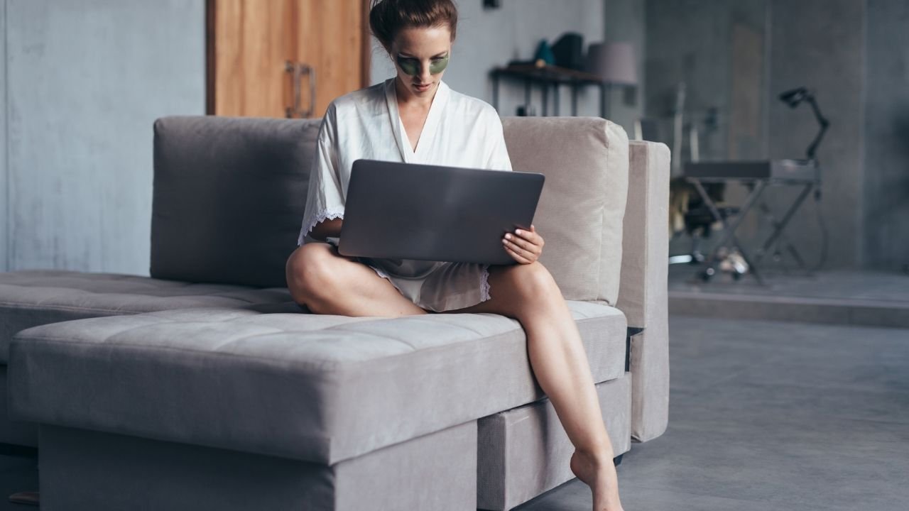 mulher com robe branco usando notebook no sofá